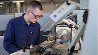 A Soldier in blue overall works at a lathe.