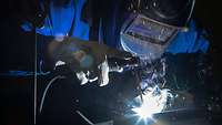 A soldier in a blue overall is welding a square object.
