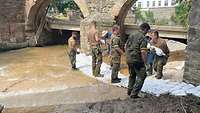 Soldaten und Angehörige des THW bauen einen Damm aus Sandsäcken.