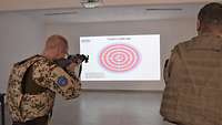 Ein Soldat zielt mit einem Sturmgewehr auf eine an die Wand projizierte Zielscheibe