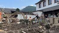 Soldaten und Zivilpersonen entrümpeln ein Haus, Schlamm vor der Türe