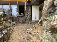 Zwei Soldaten stehen tief im Schlamm und räumen Schutt aus einem Gebäude