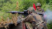 Ein Soldat schießt mit einem Panzerfaustschießgerät, der Sicherheitsgehilfe schaut ihm dabei zu.