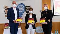 Ministerin Kramp-Karrenbauer, ein Soldat und ein Mann stehen nebeneinander und halten ein Buch in der Hand