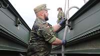 Zwei Soldaten arbeiten an den dunkelgrünen Brückenteilen des Brückenlegepanzers.