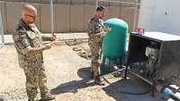 Zwei Soldaten stehen an einem Wassertank. Sie entnehmen Wasserproben und dokumentieren dies