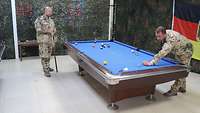 Zwei Soldaten spielen in einem Bereich, der mit Tarnnetzen abgehangen ist Billard. Die Wiese des Billardtisches ist blau