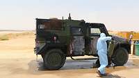 Ein Soldat in blauem Schutzanzug besprüht ein Fahrzeug