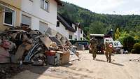 Ein Trupp aus zwei Soldaten im Katastrophengebiet. Einer trägt einen Rucksack mit rotem Kreuz darauf.