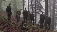 Mehrere Soldaten stehen an einem Waldhang bei Nebel und schauen ins Gelände.