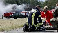 Ein deutscher Feuerwehrmann und ein österreichischer Notfallsanitäter knien über einem Übungsverletzten.