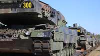 Ein Kampfpanzer wird von einem Wagon heruntergefahren. Ein Soldat prüft, dass der Panzer genau mittig über den Waggon fährt