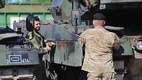 Ein deutscher und ein niederländischer Soldat prüfen einen Kampfpanzer auf mögliche Beschädigungen.