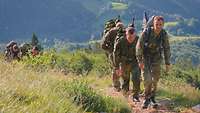 Mehrere Soldaten marschieren hintereinander einen Wanderweg bergauf.