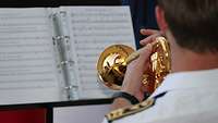 Ein Musiker spielt eine goldene Trompete. Im Hintergrund ist ein Notenheft zu sehen.
