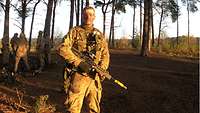 Fähnrich Hilscher steht mit seinem Gewehr auf einer Waldlichtung.