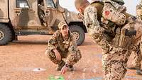 Ein Soldat hockt vor einem Soldaten auf dem Boden und erklärt mit seinen Händen eine Skizze, die auf die Erde aufgesprüht wurde