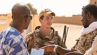 Ein Soldat spricht mit einem Sprachmittler und einem Bewohner eines afrikanischen Dorfes