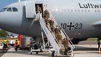 Mehrere deutsche Soldaten verlassen über eine Treppe ein graues Passagierflugzeug auf einem Flugplatz.