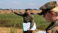 Mit der Karte in der Hand stehen zwei deutsche Soldaten draußen auf einem grünen Feld. 