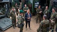 Eine Zivilistin steht zwischen grünen Containern eines Gefechtsstandes neben mehreren Soldaten in Uniform.