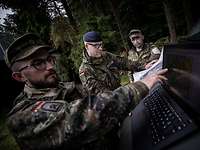 Soldaten mit einer Karte und einem Laptop stehen während einer Übung auf einer Waldlichtung und besprechen sich.