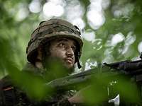 Soldat mit Tarnschminke auf seinem Alarmposten mit einem Maschinengewehr 3 auf einem abgetarnten geländegängigen Lkw.