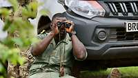 Ein malischer Soldat sitzt mit einem Fernglas vor den Augen an ein Auto gelehnt