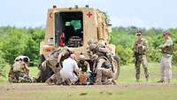 Mehrere Soldaten und Sanitäter vor einem gepanzerten Sanitätsfahrzeug kümmern sich um zwei Verwundete.