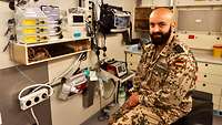 Ein Soldat sitzt auf der Liege eines Sanitätscontainers. Im Hintergrund medizinische Geräte
