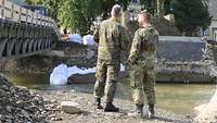 Zwei Soldaten stehen mit dem Rücken zur Kamera am Flussbett der Ahr.