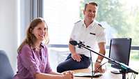Lehrgangsteilnehmende des LGAN 2019 Regierungsdirektorin Martina Schmitz und Korvettenkapitän Boris Melching sitzen vor dem Podcast-Mikrophon am Schreibtisch