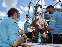 Ein Geretteter zeigt sein Ausweispapier weiteren Soldaten in blauer Uniform.