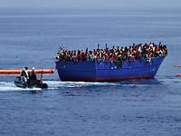 Ein blaues Boot mit vielen dunkhäutigen Menschen treibt auf offener See.