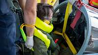 Ein Pilot in einem Cockpit, der von Helfern daraus befreit wird.