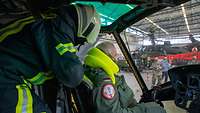 Ein Pilot im Cockpit eines Hubschraubers, hinter ihm ein Feuerwehrmann.
