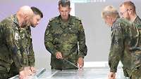 Ein Soldat steht mit vier weiteren Soldaten um einen Kartentisch und zeigt mit einem Zeigestock auf eine Karte.