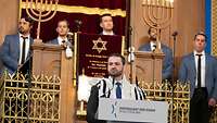 Ein Mann spricht an einem Rednerpult mit der Aufschrift „Zentralrat der Juden in Deutschland“ in einer Synagoge