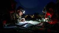 Drei Soldaten liegen auf der Erde in der Mitte eine Karte mit Schreibzeug.