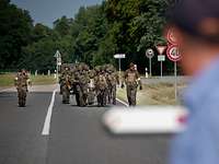 Mehrere Soldaten in komplettem Kampfanzug tragen einen verletzten Kameraden auf einem Tragetuch in Richtung Kasernentor.
