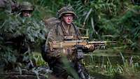 Ein Soldat mit komplettem Gefechtsanzug und Waffe steht in einem Gewässer.