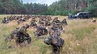 Zahlreiche Soldaten knien zum Gebet vor dem Pfarrer auf einer Waldlichtung.