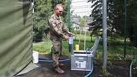 Ein Soldat füllt eine Wasserprobe aus einem Hahn in einen Messbecher.
