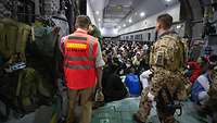Viele evakuierte Personen sitzen im Laderaum eines A400M, ein Soldat und ein Mann stehen davor auf der Laderampe