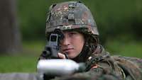 A soldier is taking aim through the telescopic sight of a rifle.