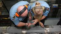 Two soldiers work on an engine.