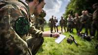 Viele Soldaten stehen im Gelände und werten eine Lage aus.