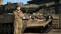 Oberfeldwebel J. steht mit verschränkten Armen vor einem Panzer.