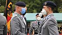 Zwei Soldaten stehen sich gegenüber und reichen sich neben einer Fahne die Hand.