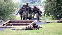 Soldaten tragen einen Verwundeten, andere liegen mit dem Gewehr am Boden und sichern sie ab.